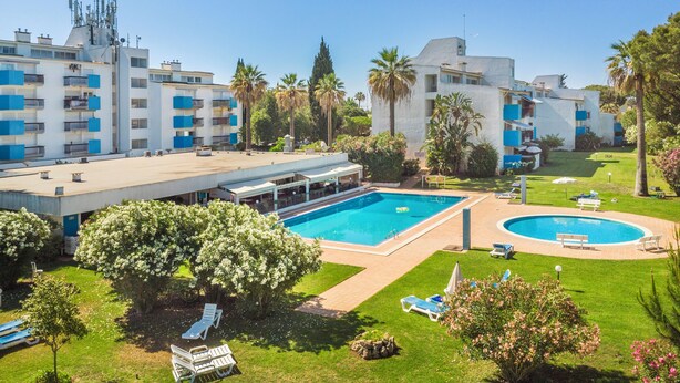 Um hotel com várias piscinas, área externa coberta e vegetação exuberante.
