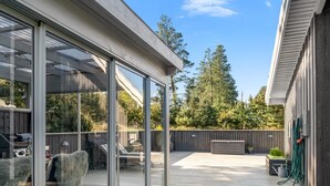 Eine überdachte Terrasse mit Glasverkleidung, Holzdeck, Gartenmöbeln und einem Grill.