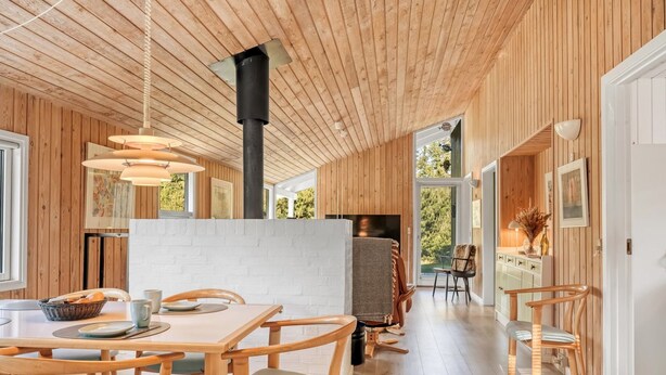 Ein modernes Interieur mit Holzvertäfelung, einem zentralen Kamin und einem Essbereich mit Tageslicht.