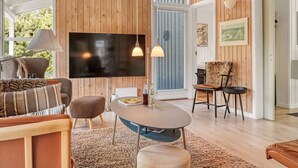 Ein modernes Wohnzimmer mit großem Flachbildfernseher, Holzwandverkleidung, einem runden Couchtisch und einer gemütlichen Sitzecke mit Sofa und Hocker.
