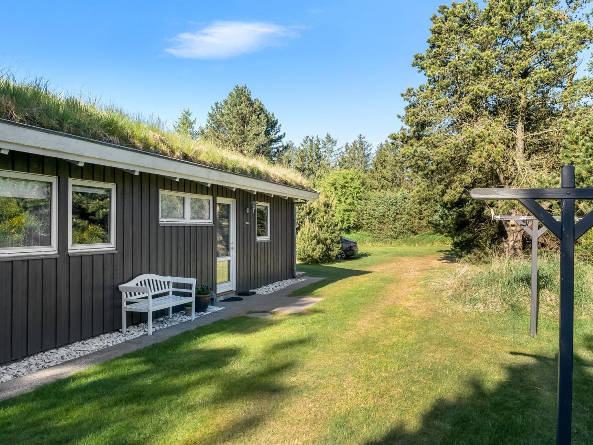 Eine moderne Holzhütte mit einem grünen Dach, einer Bank davor und einem Weg zum Eingang.