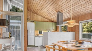 Eine moderne Küche mit Holzausstattung, ein Essbereich mit Holztisch und Stühlen sowie ein großes Fenster, das für natürliches Licht sorgt.