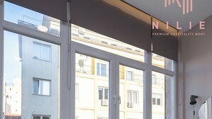 Una habitación de hotel moderna con un ventanal grande, dos taburetes negros, un escritorio de madera y una cama.