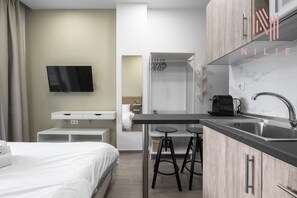 A modern hotel room with a bed, a TV, a kitchenette with a sink, and a small table with stools. - Fragkon 24 Nilie Hospitality MGMT (Thessaloniki)