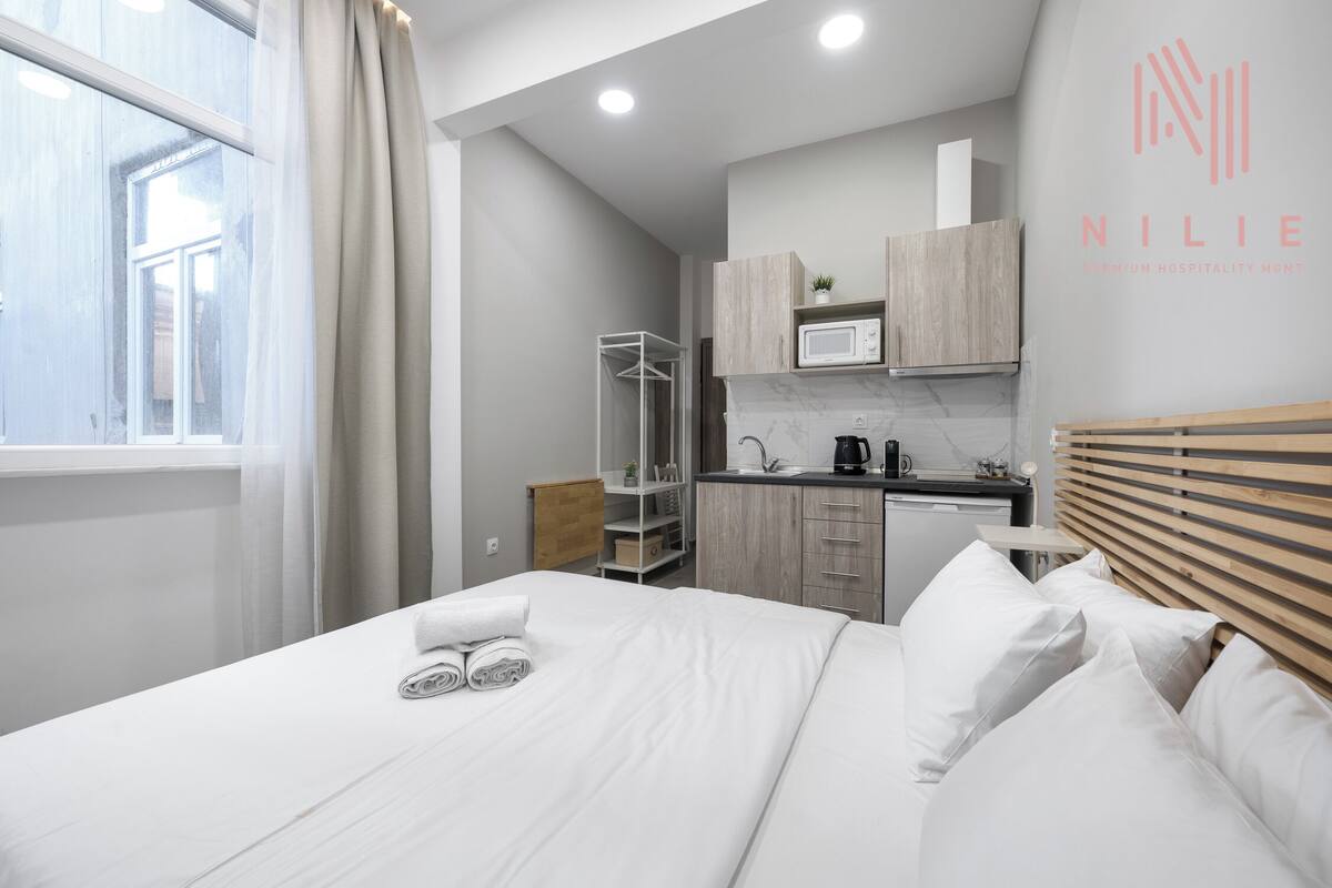 A modern hotel room with a neatly made bed, a small kitchenette, and a view of the outside.
