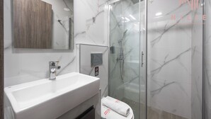 Un baño moderno con un lavamanos grande, una cabina de ducha de vidrio y una pared de mármol.