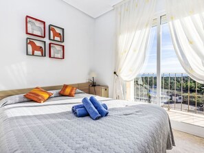 Un dormitorio con una cama grande, vistas a vegetación y un edificio a través de la ventana, y cuadros en la pared.