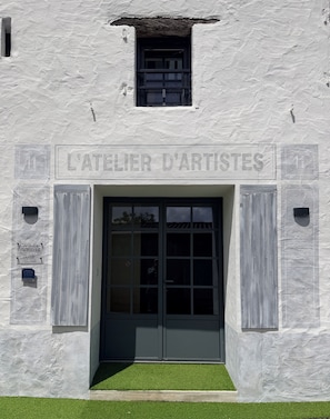 Eine Gebäudefassade mit einem Schild, auf dem 'L'ATELIER D'ARTISTES' steht, und einer Tür mit Glasscheiben.