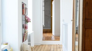 A hallway with a wooden floor, a round woven rug, a wicker basket, and a chair.