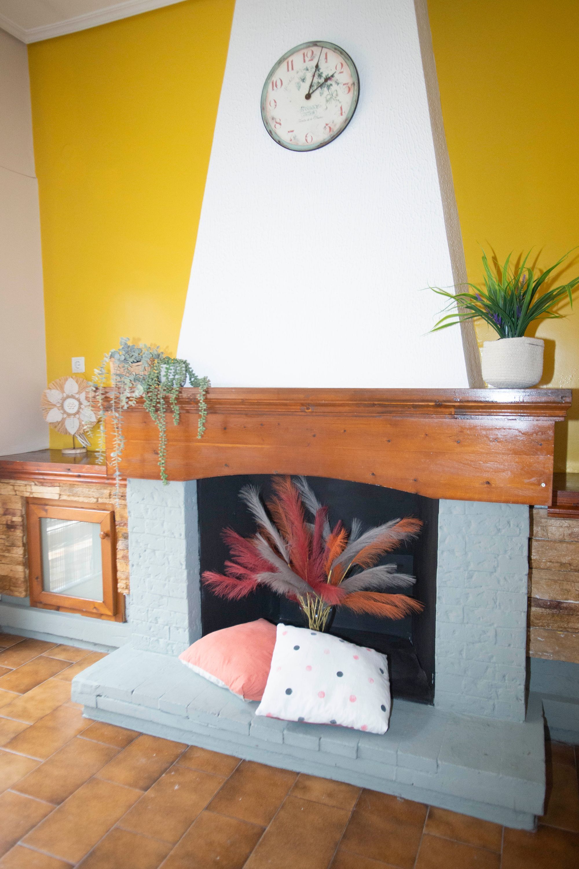A room with a fireplace, a clock on the wall, and a plant on the mantel.
