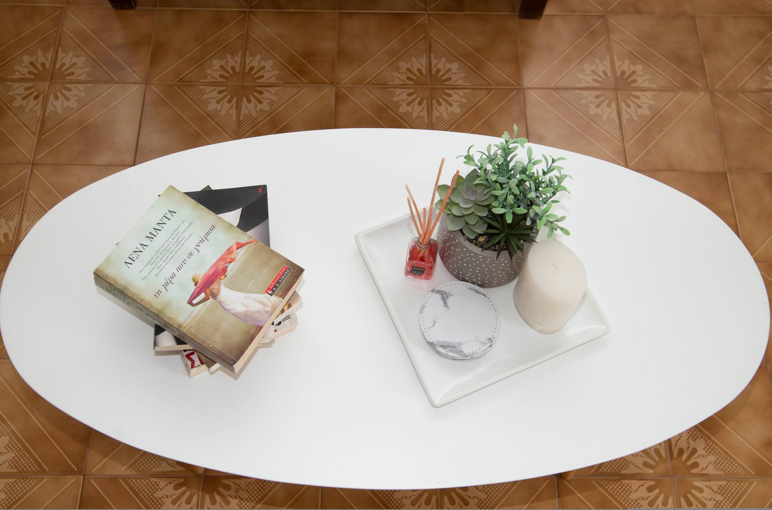 A white table with a book, a potted plant, a small vase with red flowers, and a white candle.