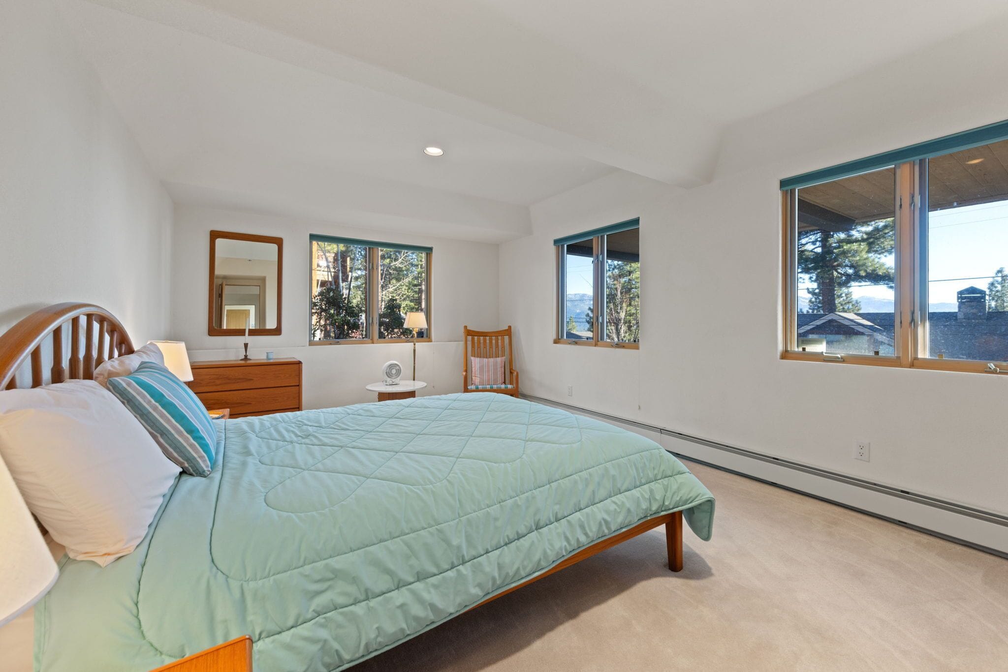 A bedroom with a bed, a nightstand, a chair, two windows, and a mirror.