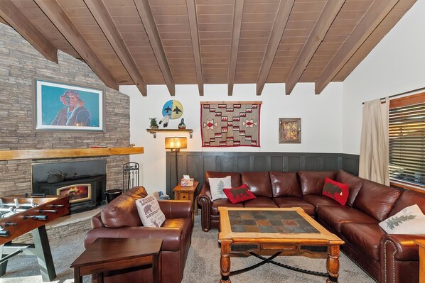 Una sala de estar con chimenea de piedra, sofás de cuero, una mesa de centro y techo de madera.