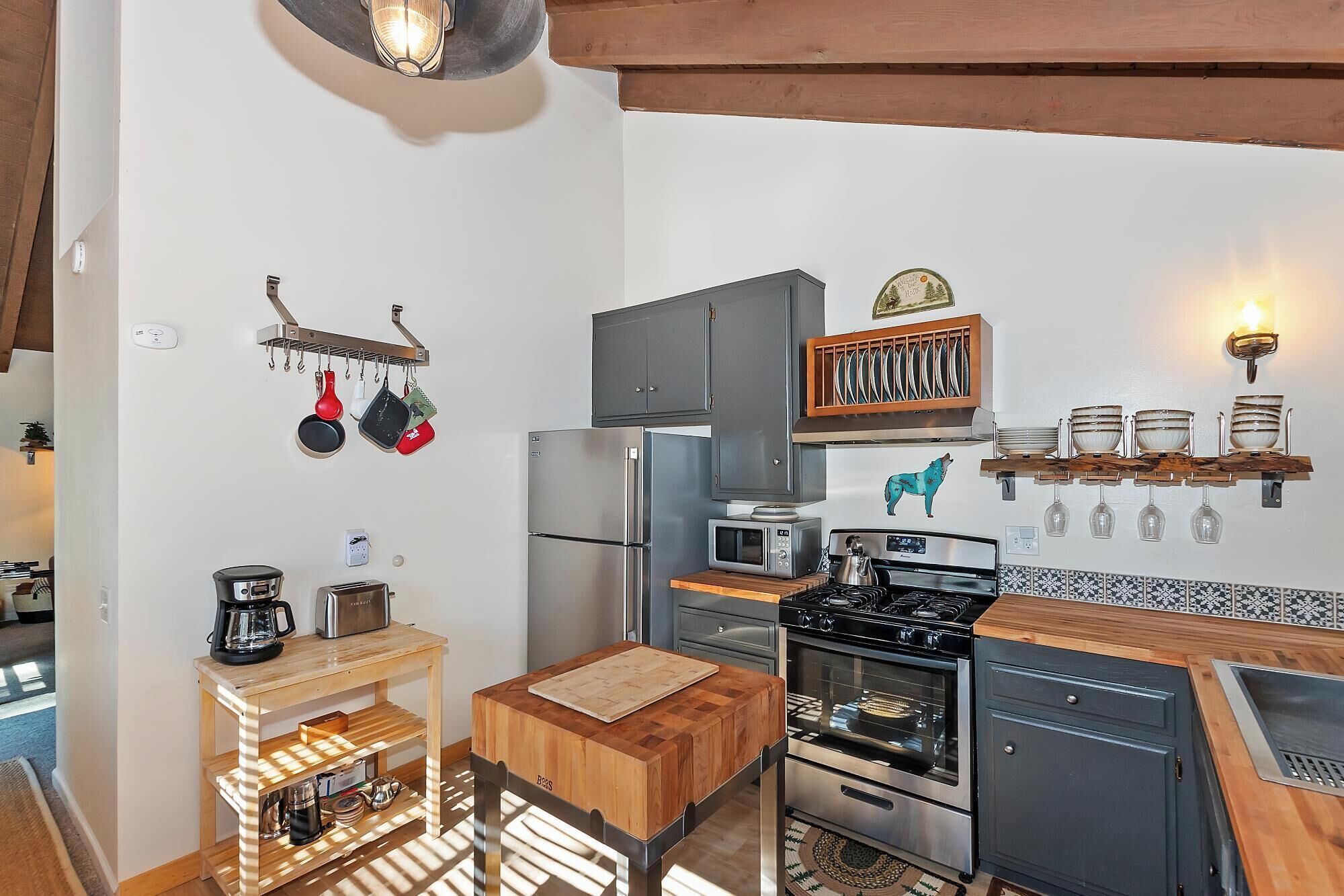 Een kleine keuken met moderne apparatuur, houten aanrecht en een hangende rek voor pannen.