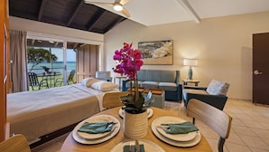 A hotel room with a bed, a dining table set for two, a sofa, a chair, a ceiling fan, and a view of the ocean through a sliding door. - Kuleana Club - 107 (Lahaina)