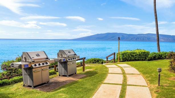 A patio with two barbecue grills, a pathway, and a view of the sea and mountains. - Kuleana Club - 107 (Lahaina)