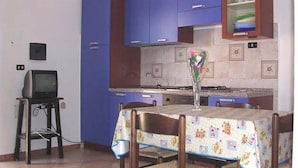 Een kleine keuken met blauwe kastjes, een houten tafel met tafelkleed en een televisie op een meubel.
