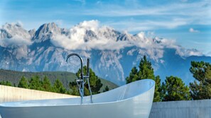 A modern bathroom with a large, curved bathtub and a faucet, set against a backdrop of mountains and a clear sky. - Shangri-La ManXinYu Frozen Dream Forest (Deqin)