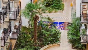 A multi-level residential building with balconies, a central courtyard with palm trees, and a tiled floor.