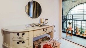 A room with a white vanity, a round mirror, and a small stool with a plant.