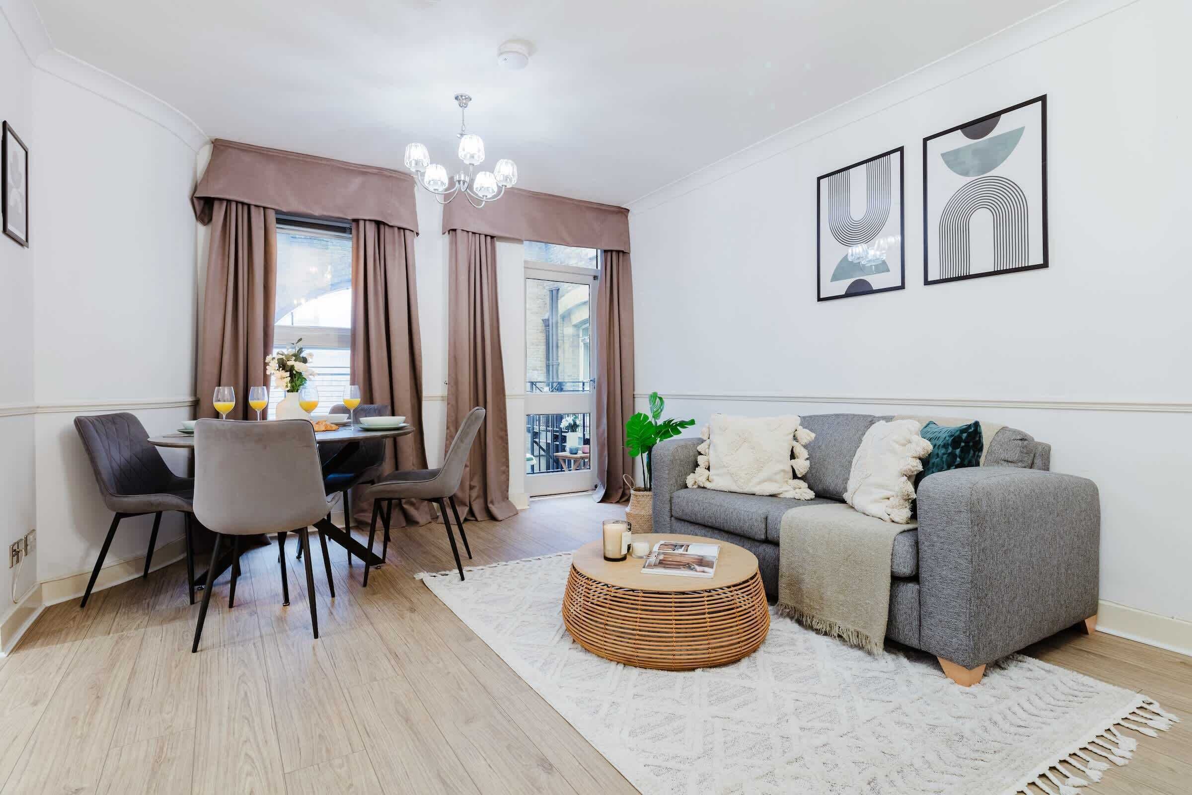 Un salon moderne avec un canapé gris, une table à manger avec des chaises, une table basse ronde et deux œuvres d’art abstraites encadrées accrochées au mur.