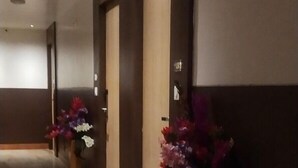 A hotel corridor with a marble floor, dark wooden doors, and floral arrangements. - Amutham Residency (Tiruchirappalli)