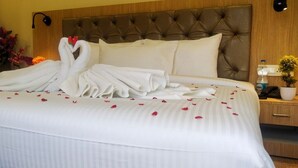 A neatly made bed with white linens, a swan-shaped towel arrangement, and rose petals scattered on the bed. - Amutham Residency (Tiruchirappalli)