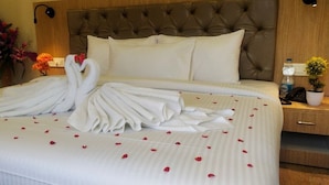 A hotel room with a large bed, a tufted headboard, a bedside table with a lamp, and a vase with flowers. - Amutham Residency (Tiruchirappalli)