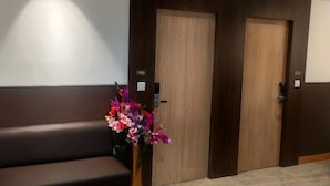 A reception area with a brown bench, a wooden reception desk, and two wooden doors with a number plate. - Amutham Residency (Tiruchirappalli)