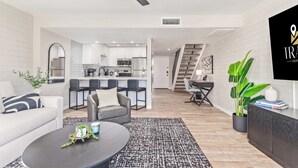 A modern living room with a sofa, coffee table, and a dining area with chairs. A kitchen is visible in the background with a staircase leading to another level. - NEW|Heatherbrae 8|Old Town|Htd. Pool|Mtn View (Scottsdale)
