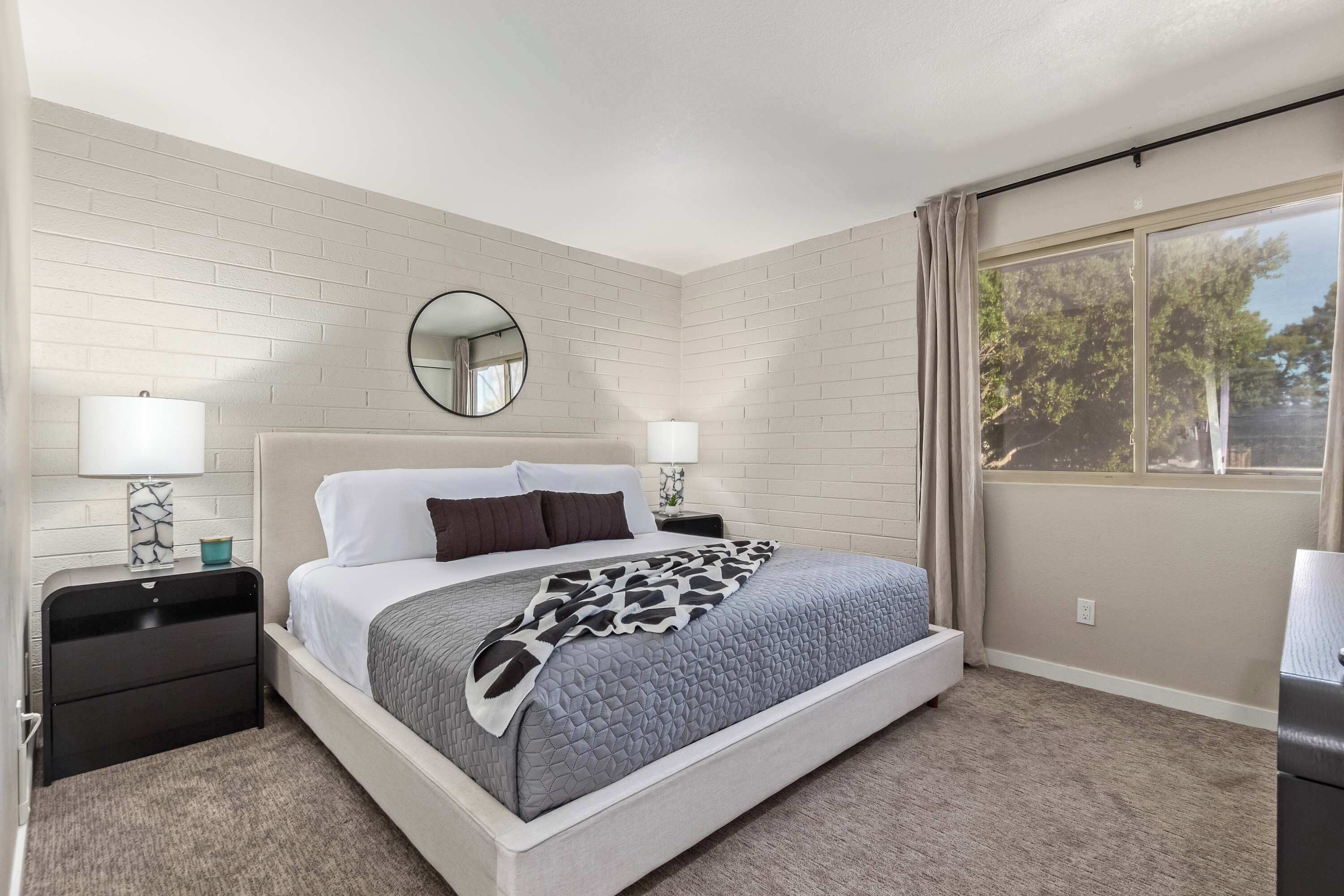 Quarto de hotel com cama, duas mesas de cabeceira, espelho e janela com cortinas.