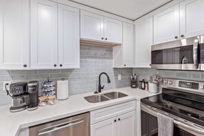 A modern kitchen with white cabinets, a stainless steel microwave, an oven, a coffee maker, and a tiled backsplash. - NEW|Heatherbrae 8|Old Town|Htd. Pool|Mtn View (Scottsdale)