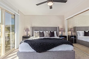 Un dormitorio moderno con una cama grande, dos mesitas de noche, un ventilador de techo y un ventanal corredero.