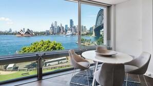A modern room with a large window overlooking a city skyline, including a distinctive bridge and a waterfront. - 'Harbourview II' – Unmatched Views of the Iconic Opera House & Harbour Bridge! (Kirribilli)