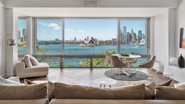 A modern living room with a large window offering a view of a city skyline and a body of water. - 'Harbourview II' – Unmatched Views of the Iconic Opera House & Harbour Bridge! (Kirribilli)
