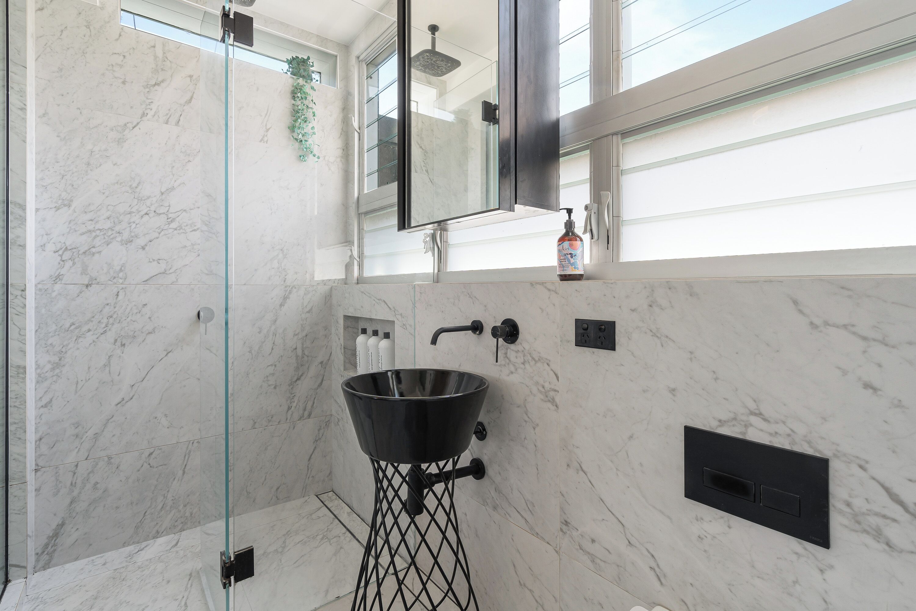 A modern bathroom with a marble wall, a glass shower enclosure, a black sink, and a large mirror. - 'Harbourview II' – Unmatched Views of the Iconic Opera House & Harbour Bridge! (Kirribilli)
