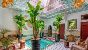 Ett rymligt inomhusområde med ett klinkergolv, stora krukväxter, en pool och traditionell inredning.