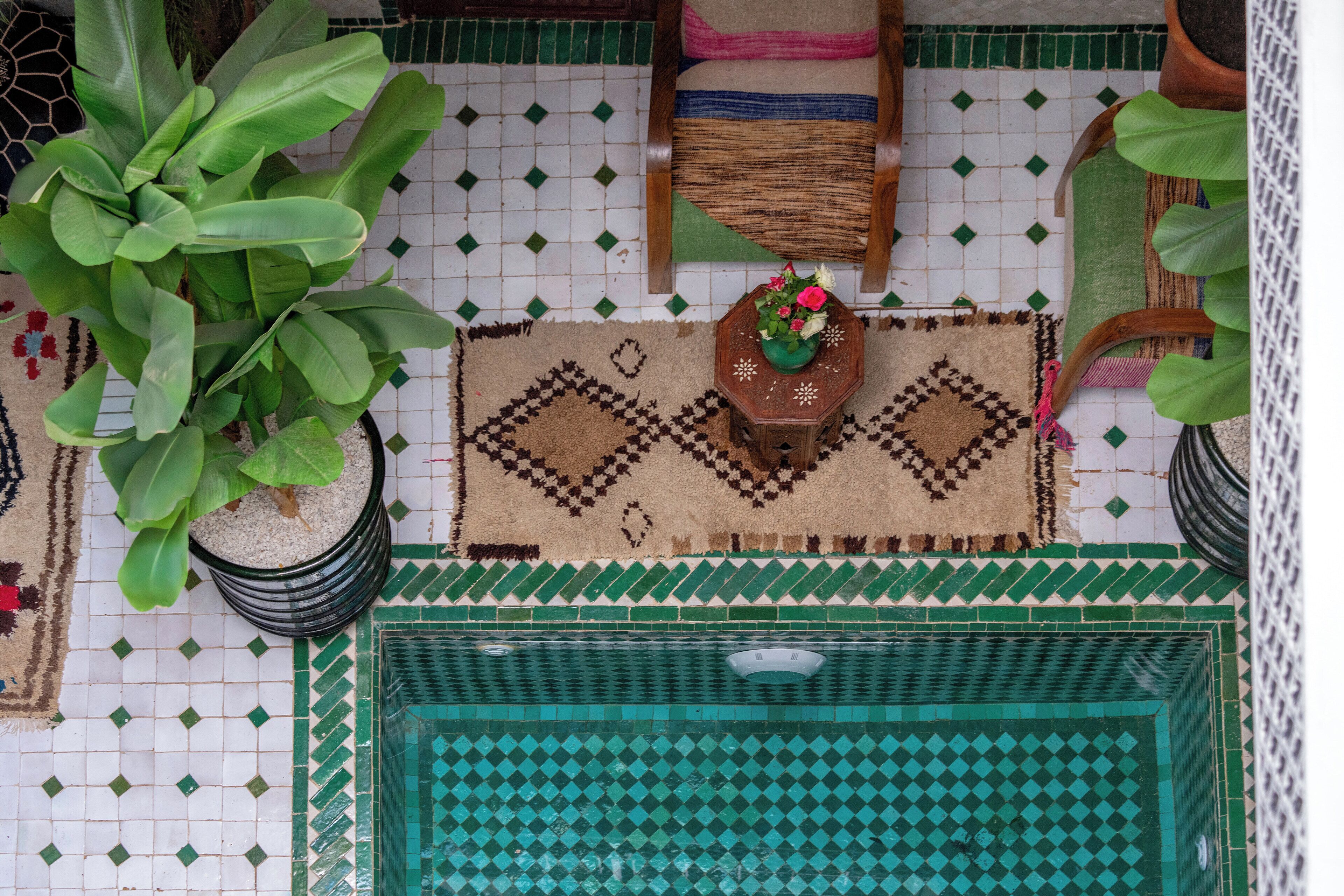 A tiled floor with a geometric pattern, a wooden chair with a woven cushion, a small wooden table with a vase of flowers, and a potted plant.