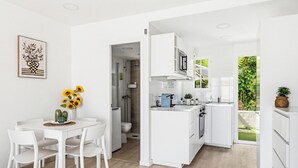 A modern kitchen with white cabinetry, a dining area with a white table and chairs, and a view of a garden through a glass door. - Castellsol 315 (Arenal d´en Castell)