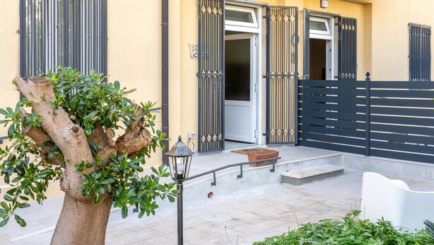 Un bâtiment à la façade jaune, avec une porte noire et un arbre au premier plan.