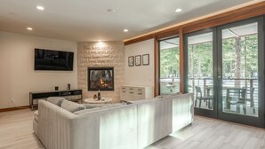 A modern living room with a fireplace, a sofa, a coffee table, and a large sliding glass door leading to an outdoor patio. - Private Hot Tub | Near Eagle Lodge (Mammoth Lakes)