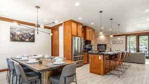 A modern kitchen with wooden cabinets, a stainless steel refrigerator, and a dining area with a wooden table and chairs. - Private Hot Tub | Near Eagle Lodge (Mammoth Lakes)