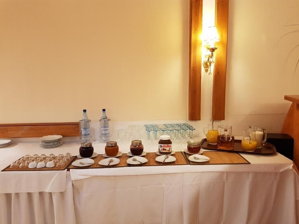 A breakfast buffet setup with various food items and beverages, including jars of jam and Nutella, a tray of orange juice, and a selection of glasses.