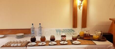 A breakfast buffet setup with various food items and beverages, including jars of jam and Nutella, a tray of orange juice, and a selection of glasses.