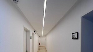 A narrow, well-lit hallway with a wooden floor, white walls, and a door at the end.