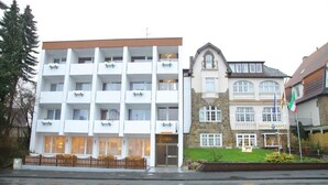 A multi-story hotel with a modern facade, a stone building with arched windows, and a flag indicating a specific country.