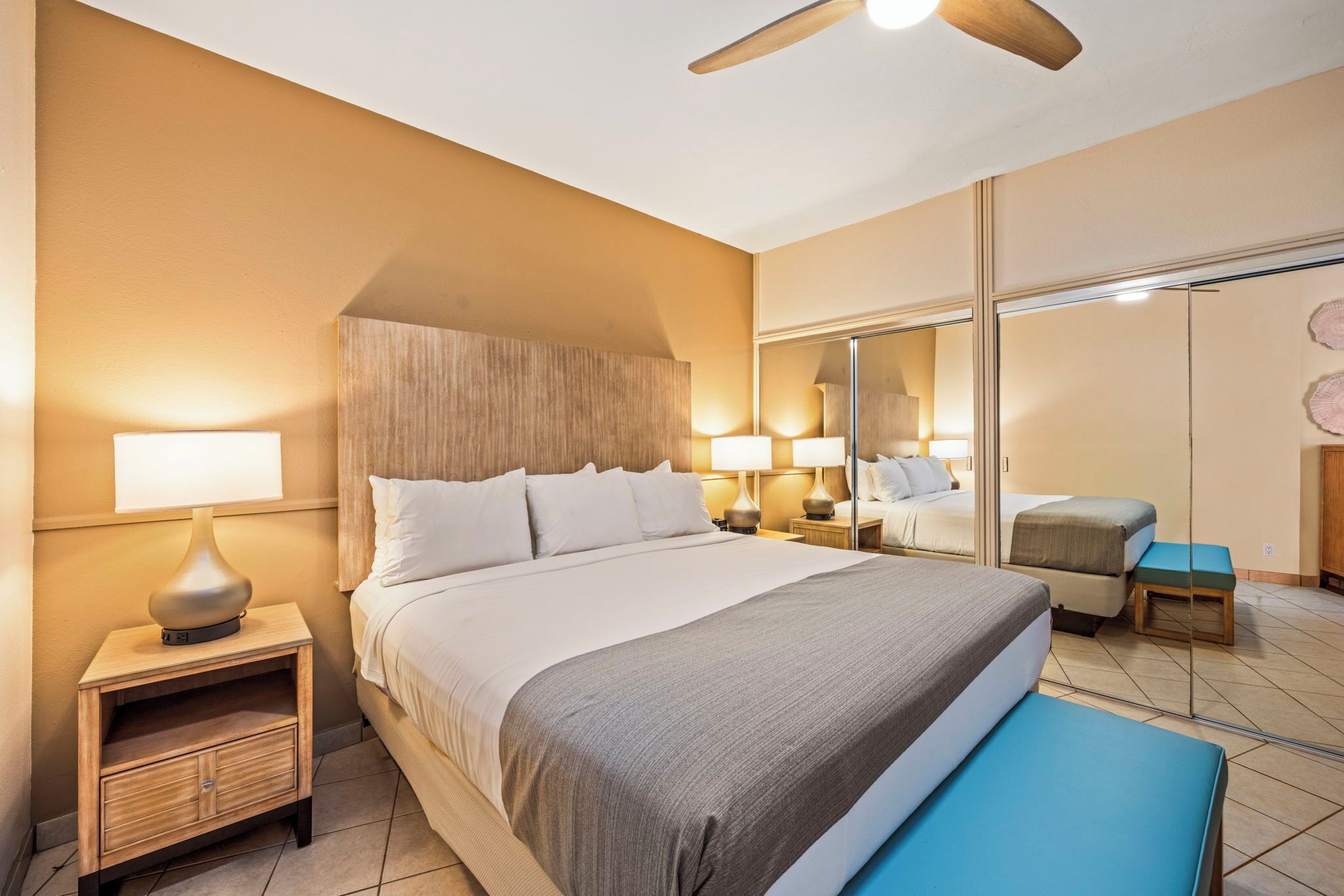 A hotel room with a large bed, bedside lamps, a nightstand, a mirror, and a ceiling fan.