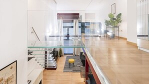 A modern interior with a glass staircase, wooden flooring, a striped rug, and a potted plant. - Easylife - Modern Comfort in Porta Venezia (Milano)