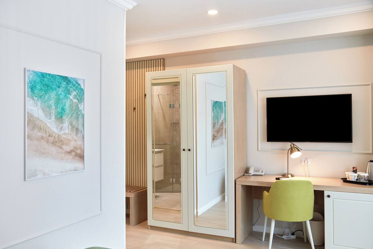 A modern hotel room with a desk, a chair, a TV, and artwork on the walls.