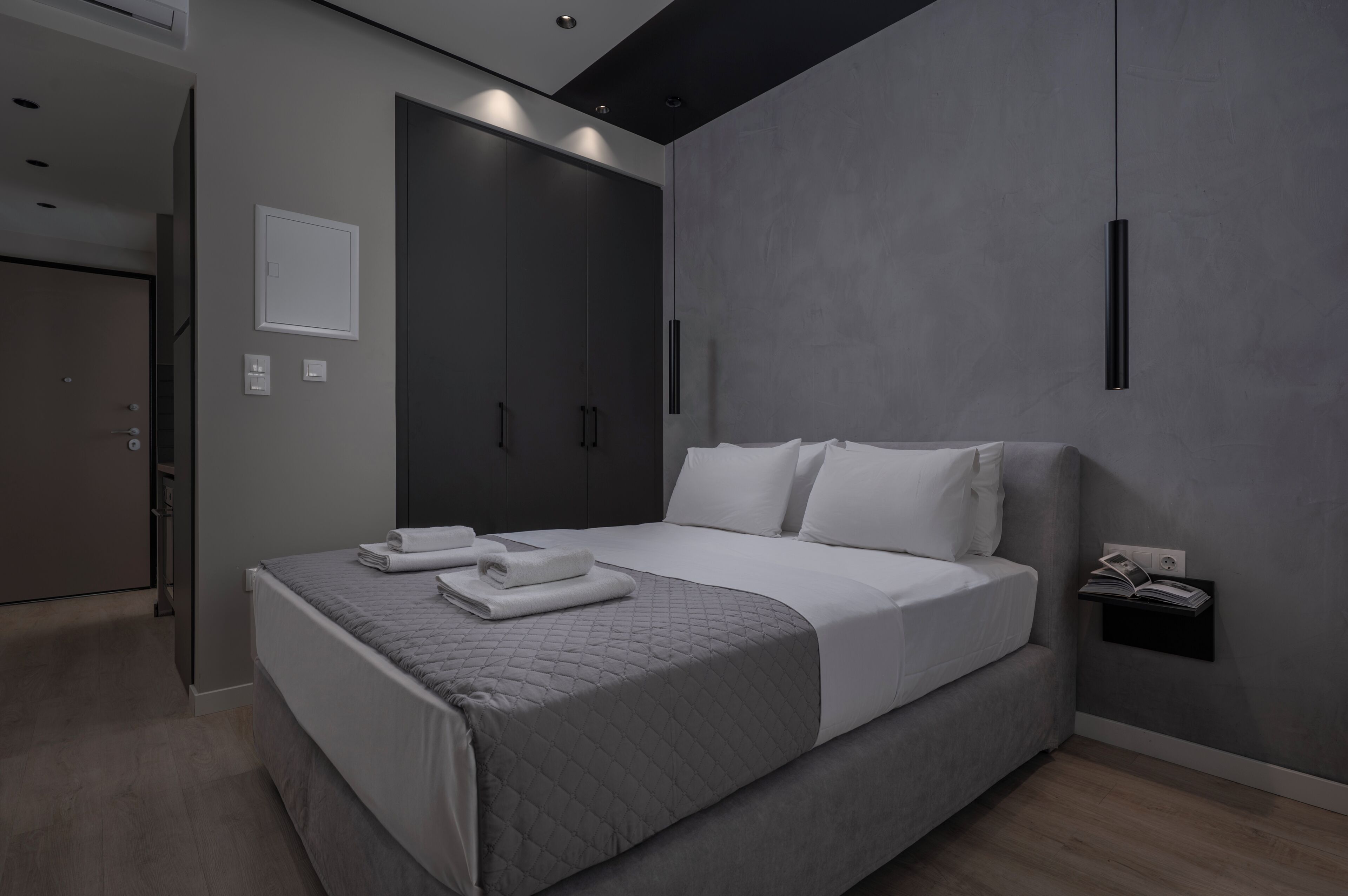 A modern bedroom with a large bed, a wardrobe, and a bedside table with a book.